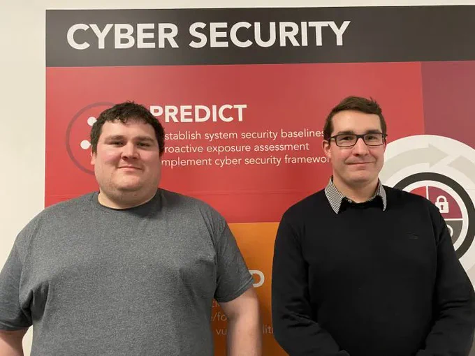 Two students standing in front of a Cyber Security sign.