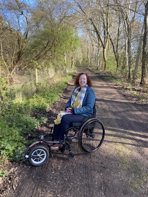 Leanne in her manual wheelchair with an attachment on the front. She’s on an unpaved track as the attachment allows the wheelchair user to go on uneven surfaces.