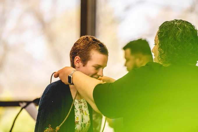 A graduate receives a rainbow cord as someone puts it around their neck