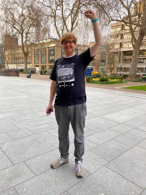 Person wearing Birkbeck University of Liberation t-shirt while lifting left fist.  