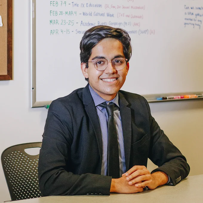 Taran Samarth, sits at a desk dressed in a suit