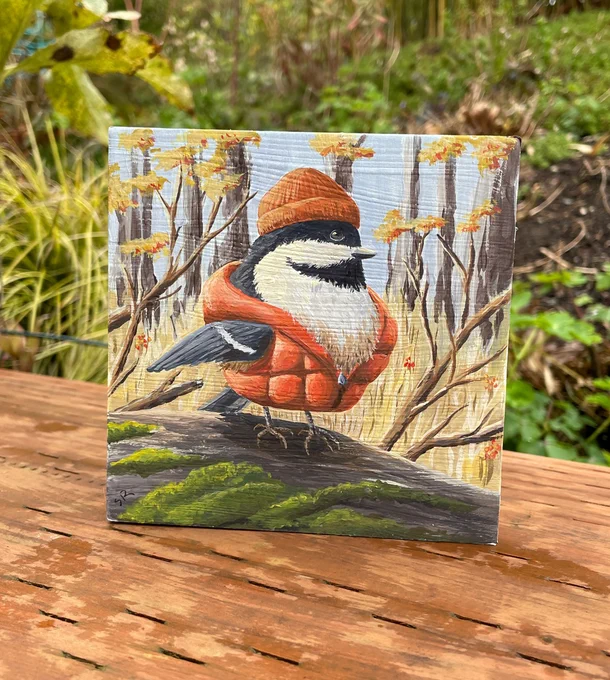 Painting of a black-capped chickadee, wearing an orange puffy jacket and knit hat. The painting is square and displayed outdoors on a wood support.