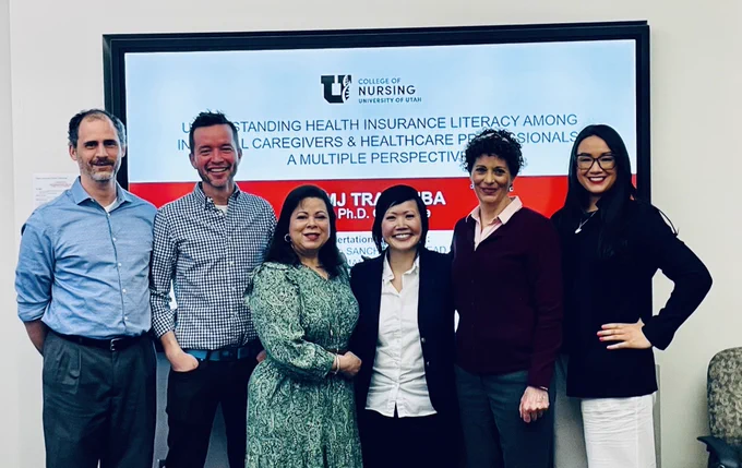MJ Tran standing with her dissertation committee members, 2 men and 3 women in front of MJ's dissertation title slide. All are smiling.