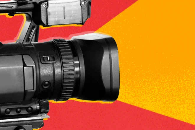 Camera lens pointed at a subject outside of the frame against red and orange background.