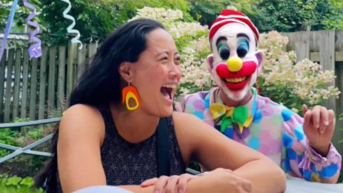 A woman laughing with someone who certainly passes for a clown but for one glaring detail: no eyes. Just dark gaping holes where eyes should be