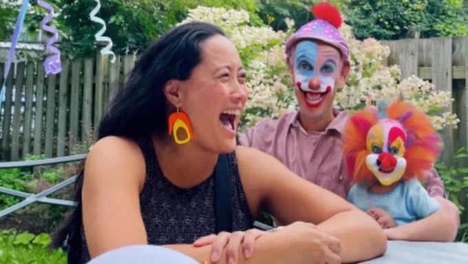 Woman laughing next to daddy and little clown with wide eyes and oddly average clothing (except the dad’s shirt looks like a golf/collar/t-shirt hybrid)