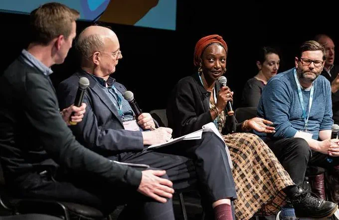 A panel on stage at the Future Of Theatre conference speaking into hand held microphones