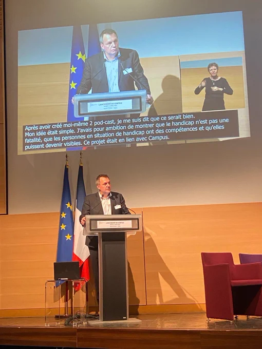Discours au pupitre de François Bernard a l’ouverture de la soirée. Derrière lui les drapeaux français et européen. Au dessus un écran avec la velotypie.