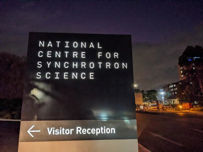 A black sign that reads "National Centre for Synchrotron Science" with an arrow pointing right to the visitor reception 