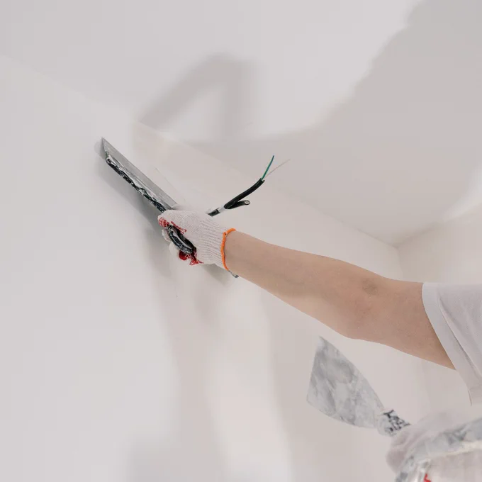 Someone plastering a white wall, around a cable. Only the person's arm, the tools and a corner of a step ladder are visible.