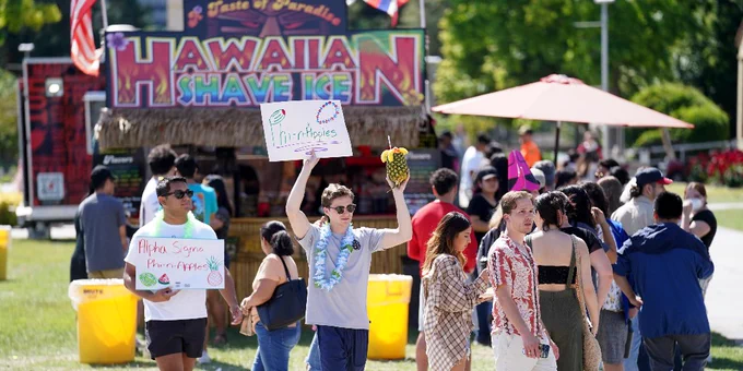 Amongst a small crowd, students hold up signs promoting the Hawaiian Shave Ice booth at Vintage Days. 