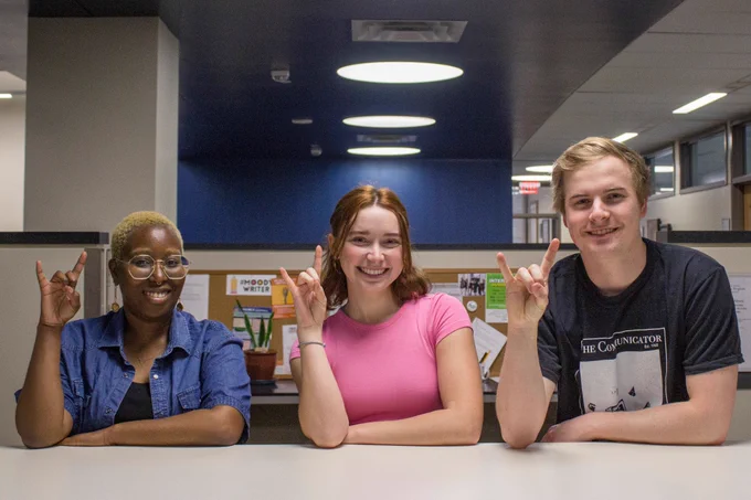 Three college students flashing the Hook 'Em Horns sign.