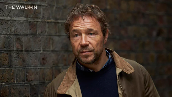 Stephen Graham as Matthew Collins in The Walk-In. He wears a brown jacket with a navy blue sweater underneath. 