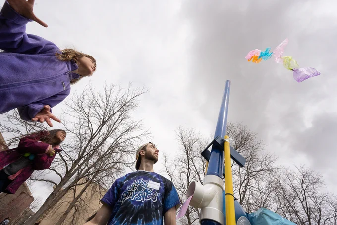 As seen from below, a kid and a Little Shop of Physics intern watch as a scarf is launched high into the air.