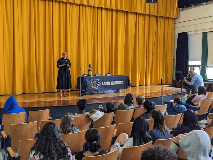 Rep. Ayanna Pressley stands on stage at the Boston Latin Academy auditorium delivering remarks during her visit. 