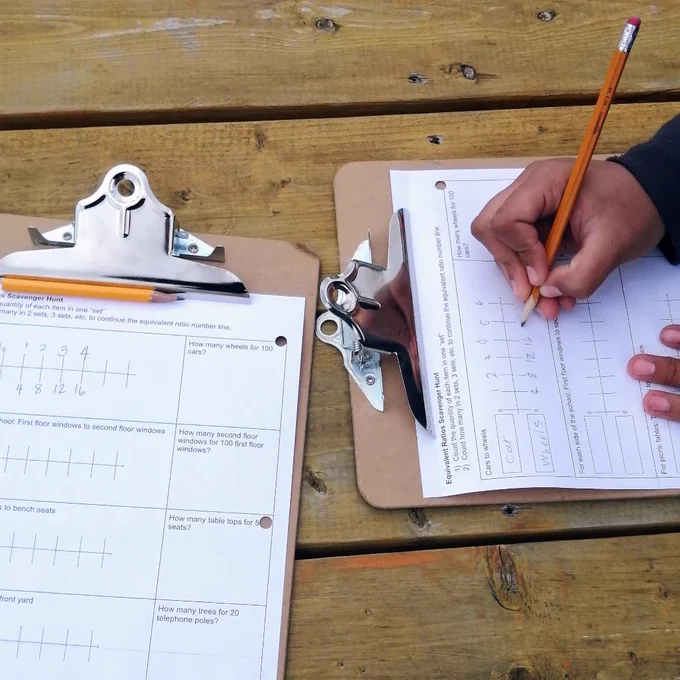 Student's hand holding pencil filling out answers on a clipboard 