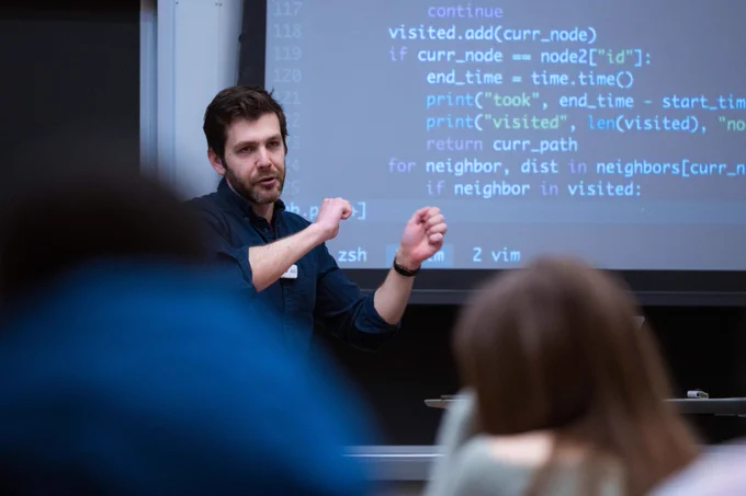 Man teaches students standing in front of screen with coding