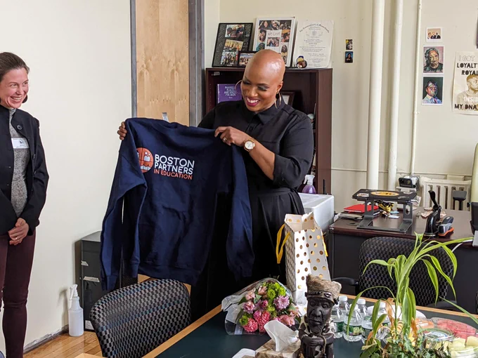 Ayanna smiling and holding up a sweatshirt that reads “Boston Partners in Education.”