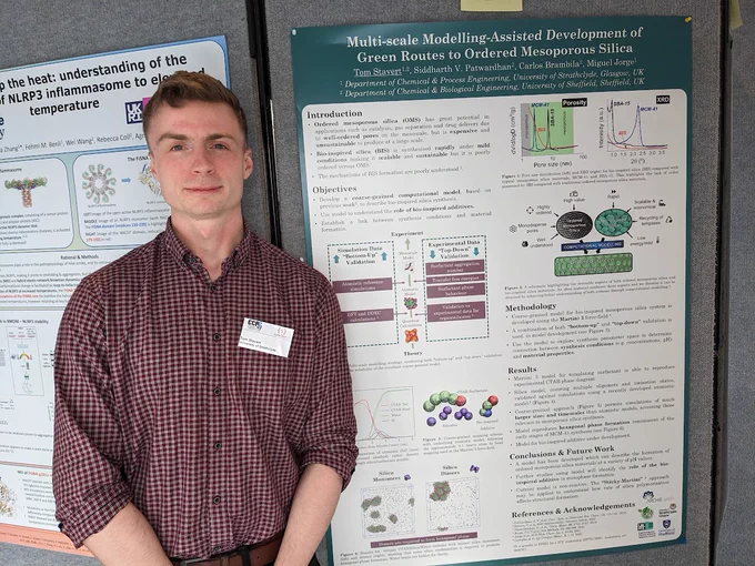 Poster prize winner Tom Stavert, a white man with short blonde hair wearing a red checked shirt, standing next to his poster.