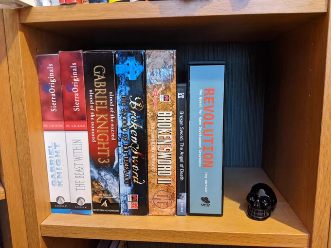 PC games in boxes on shelf alongside 'Revolution' book and small black skull ornament.