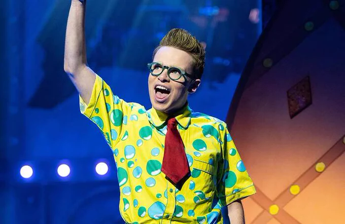 A performer in SpongeBob the Musical wearing  a yellow shirt with blue and green bubbles on and a red tie