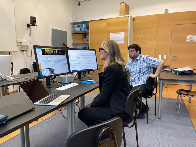 Dr. Chanda VanderHart presenting on a dual-monitor computer set up over a Zoom teleconference session, while Dr. David M. Weigl looks on
