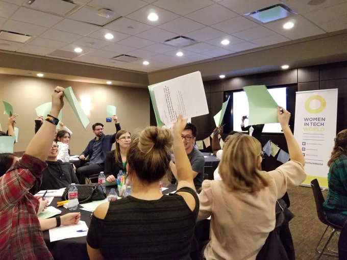 Image is of the audience sitting down at the Saskatoon community conversation. People are holding up pieces of paper with their notes on them.