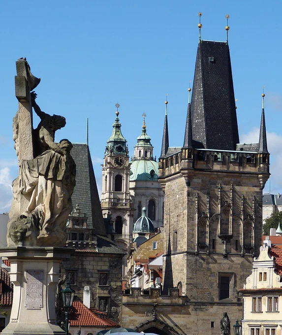 A photo of the top of a ghotic church, along with other rooftops and a sculpture, on a sunny day