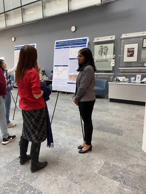 Ananya Kasi stands in front of her poster showing her research and talks to Rada Mihalcea.
