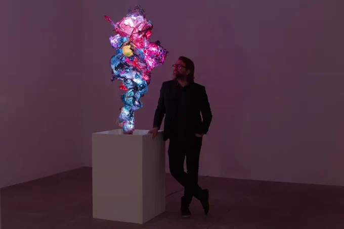 A man stands next to a tall, luminescent sculpture.