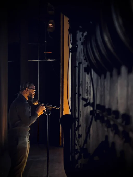 Ryan Coogler dressed in all black backstage at the SF Film Festival. Orange lighting seeps in from the stage.