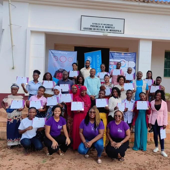 Foto de família com mulheres e homens mostrando os seus certificados após concluirem uma formação em Gestão de Higiene Menstrual. 