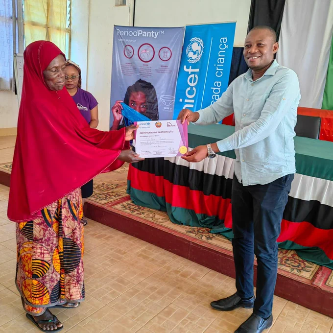 Uma mulher recebe um certificado de um homen após concluir uma formação em Gestão de Higiene Menstrual. 