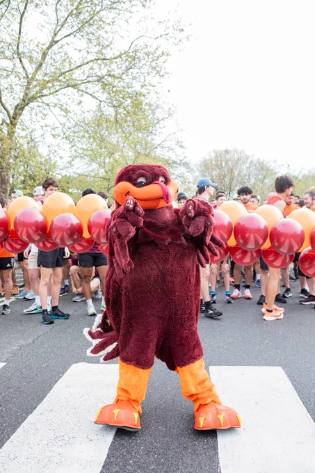 The HokieBird points in front of an orange and maroon balloon arch before the 2023 3.2-Mile Run in Remembrance.