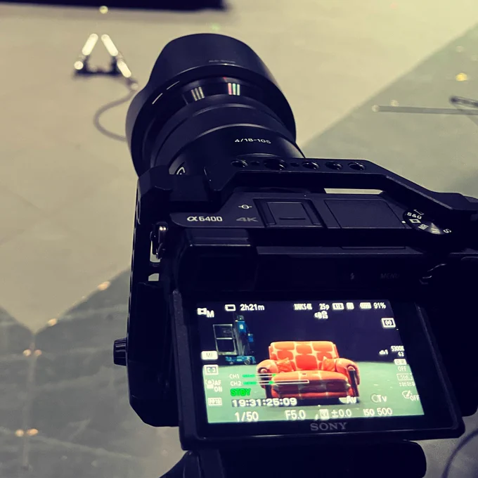 A camera onstage during setup - the view from the camera screen showing it pointing towards an orange sofa.