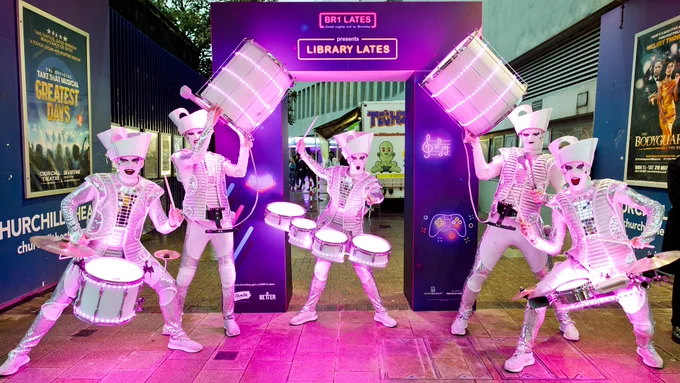 Photo of 5 Spark! Drummers in white face and outfits in front of the Library Lates arch at the entrance to Bromley Central Library.