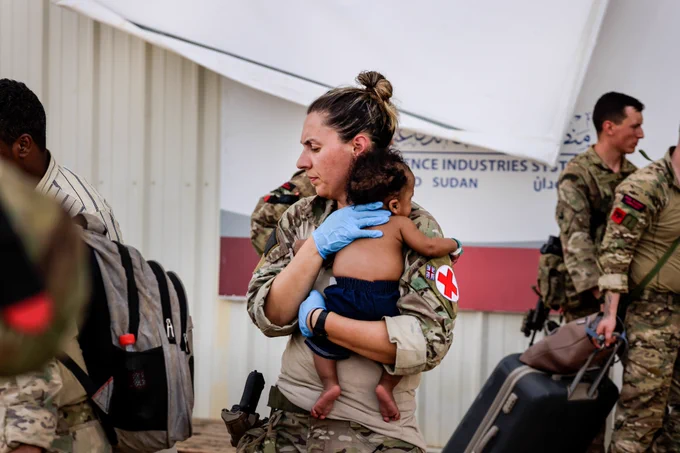 Image of an Army paramedic comforting a baby following treatment, whilst at Wadi Seidna Air Base in Sudan