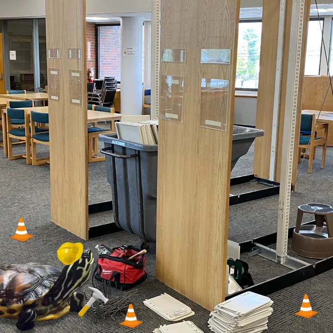 Empty bookshelves in library with a image of Fred the turtle with cartoon construction hat and cones.