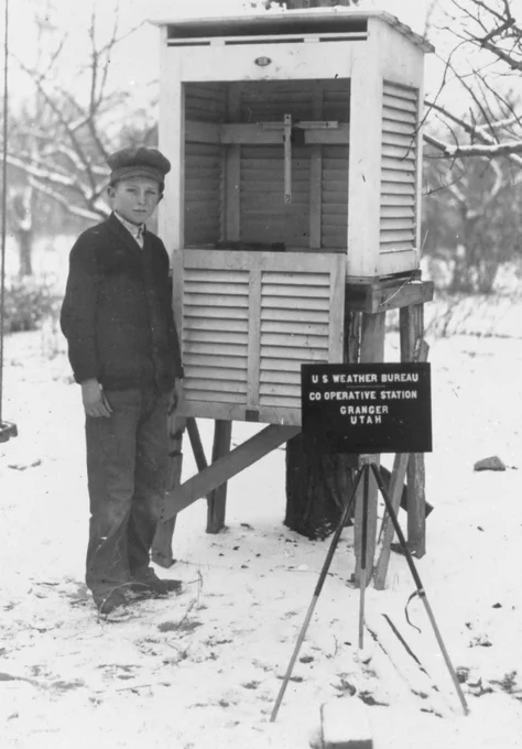 black and white photo of a boy posing in front of a small weather station
