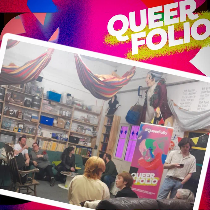 A room full of people sitting, standing, chatting, looking at phones. Sofas, shelves with props, colourful material hanging from the ceiling, Queer Folio pull up banner.