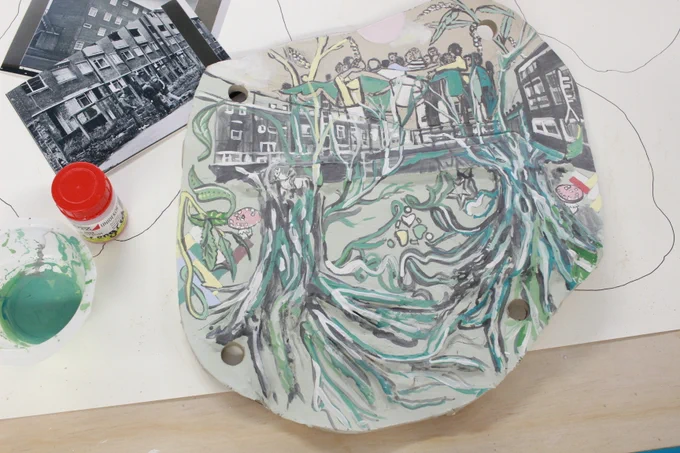 Clay sculpture with a painting of a group of people, houses and tree roots