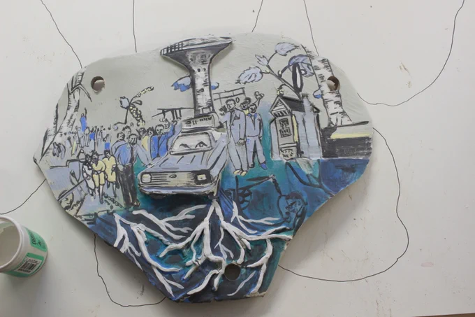 Clay sculpture with a painting of a tower and a car surrounded by people