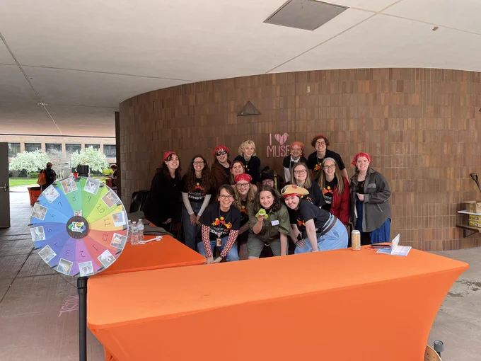 Students posed and smiling with orange cloth covered table facing camera