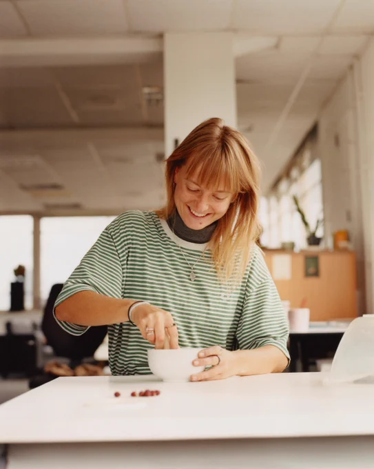 Artist Hannah Fletcher smiles while grinding berries in pestle and mortar, while in workshop