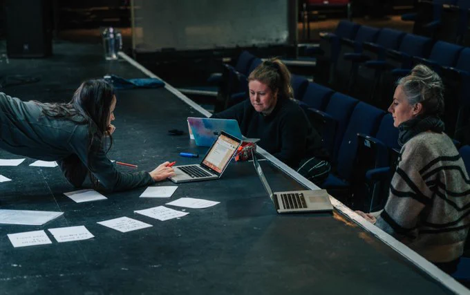 Three people gathered around notes and laptops during rehearsals in ARC's Theatre.