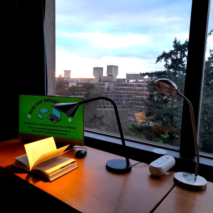 A book is illuminated by a lamp on a desk with a computer at the Library