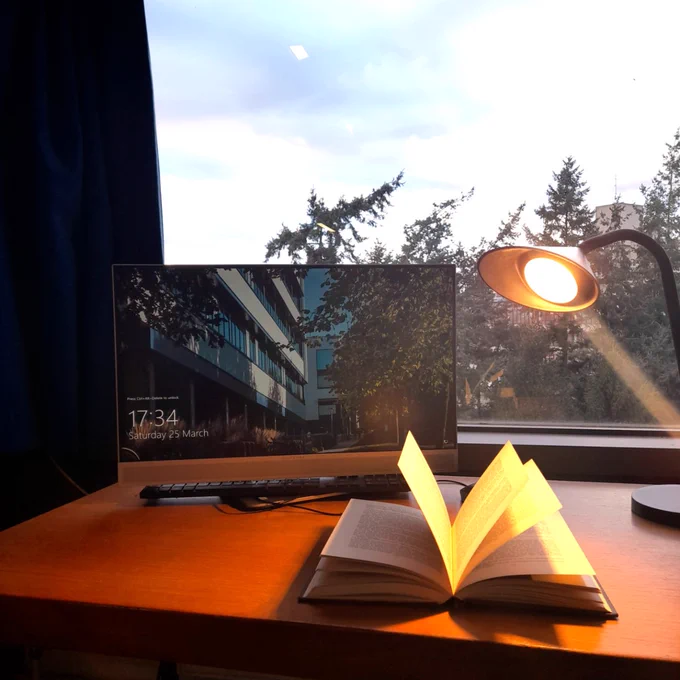 A book is illuminated by a lamp on a desk with a computer at the Library