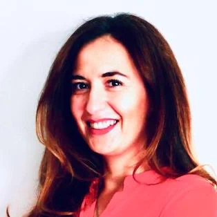An image of Cristina Dramgomir smiling. She wears a peach-color top.