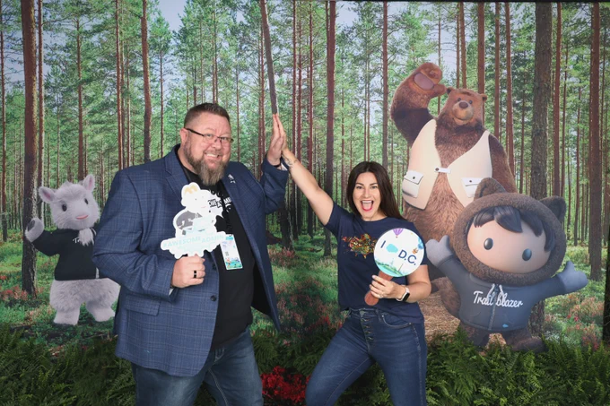 Mike Gerholdt and Lisa Dick high-fiving in front of a photo op with Cloudy, Codey, and Astro. 