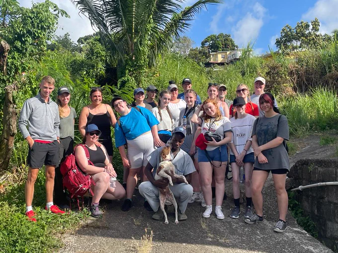 A big group of students stood smiling at the camera with a dog at the front.